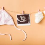 baby-s-cap-ultrasound-picture-pair-woolen-shoes-hanging-clothesline-against-orange-backdrop_23-2147900711-1